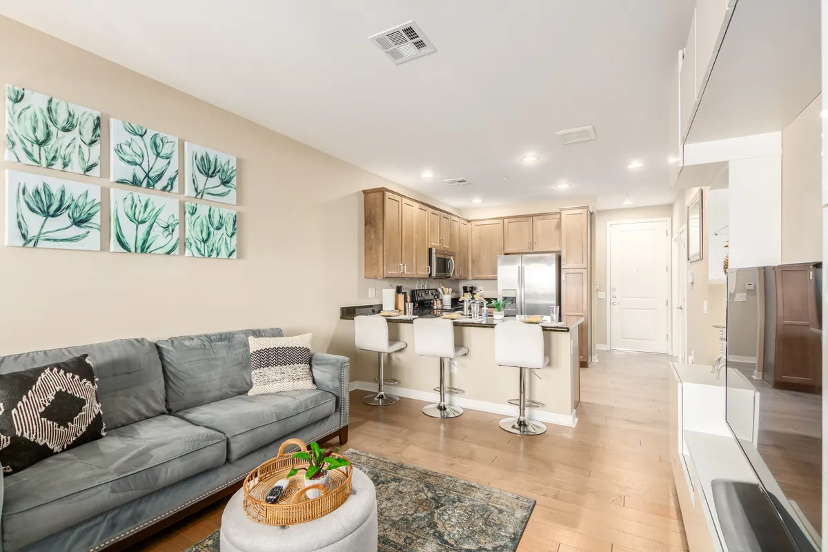 A cozy living area seamlessly connects to a kitchen island, with a sofa for relaxing and artwork on the wall. The space hints at gatherings, relaxation, and shared meals.