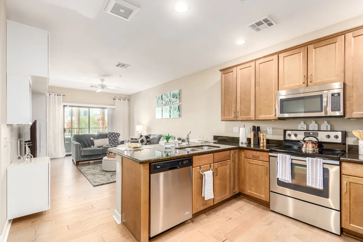 This image depicts a stylish open-concept kitchen and living room, featuring a spacious kitchen island with stainless steel appliances and decorative wall art. The living area is visible from the kitchen, emphasizing the cohesive flow between the culinary and social spaces.