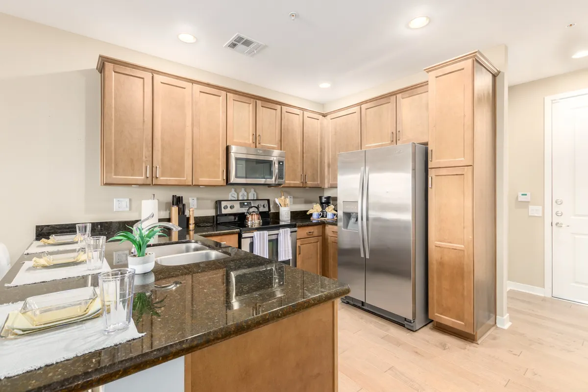 An elegant kitchen scene featuring sleek granite countertops, stainless steel appliances, and warm wood cabinetry. The kitchen is designed for both cooking and entertaining, with space for gatherings and culinary creativity.