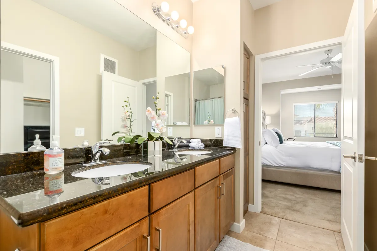 A master bathroom with an elegant double sink vanity, expansive mirrors, natural light streaming in from a window, and touches of greenery for a spa-like feel. The calm ambiance is ideal for self-care routines.