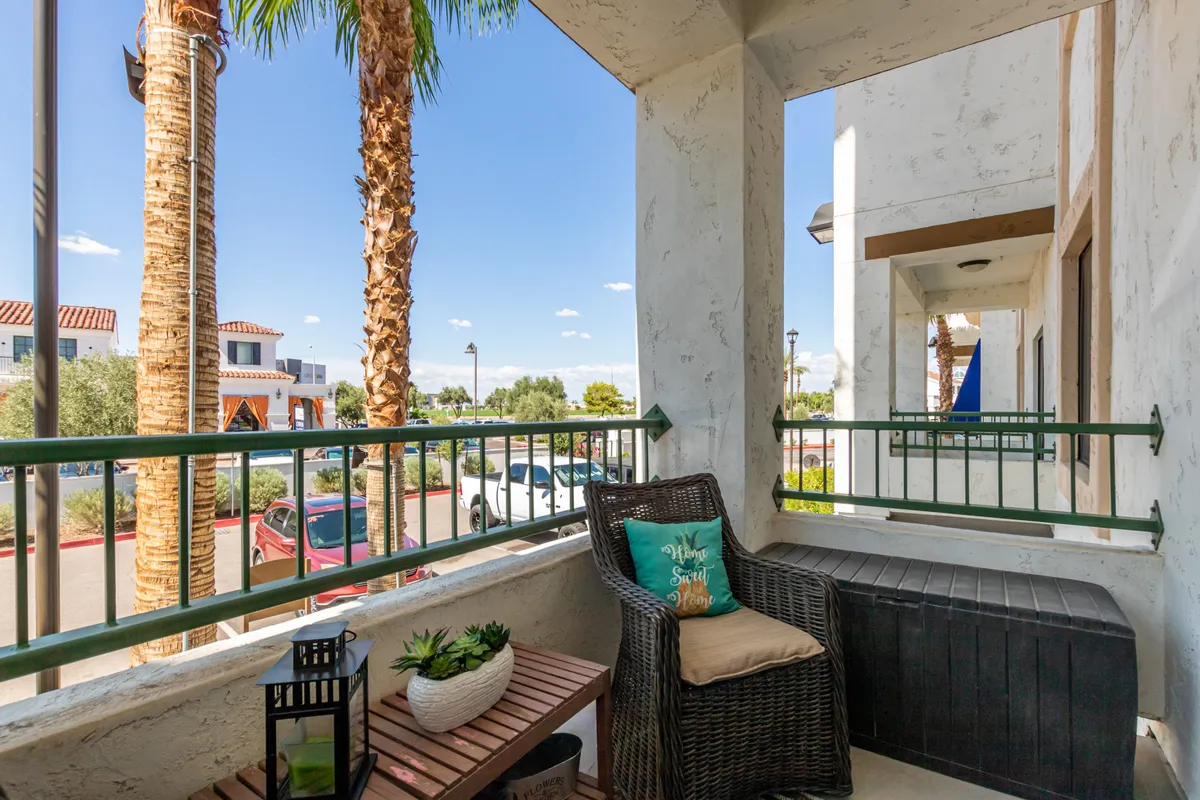 A single inviting wicker chair with a decorative pillow and a small table, surrounded by palm trees. The setting is intimate and ideal for a solitary reading session or evening drink, with an inviting, people-watching-friendly atmosphere.
