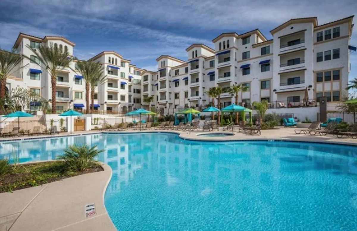 A heated swimming pool flanked by palm trees, lounge chairs, and the complex’s facade. The tranquil setting suggests a leisurely atmosphere perfect for sunbathing, swimming, or socializing by the water.