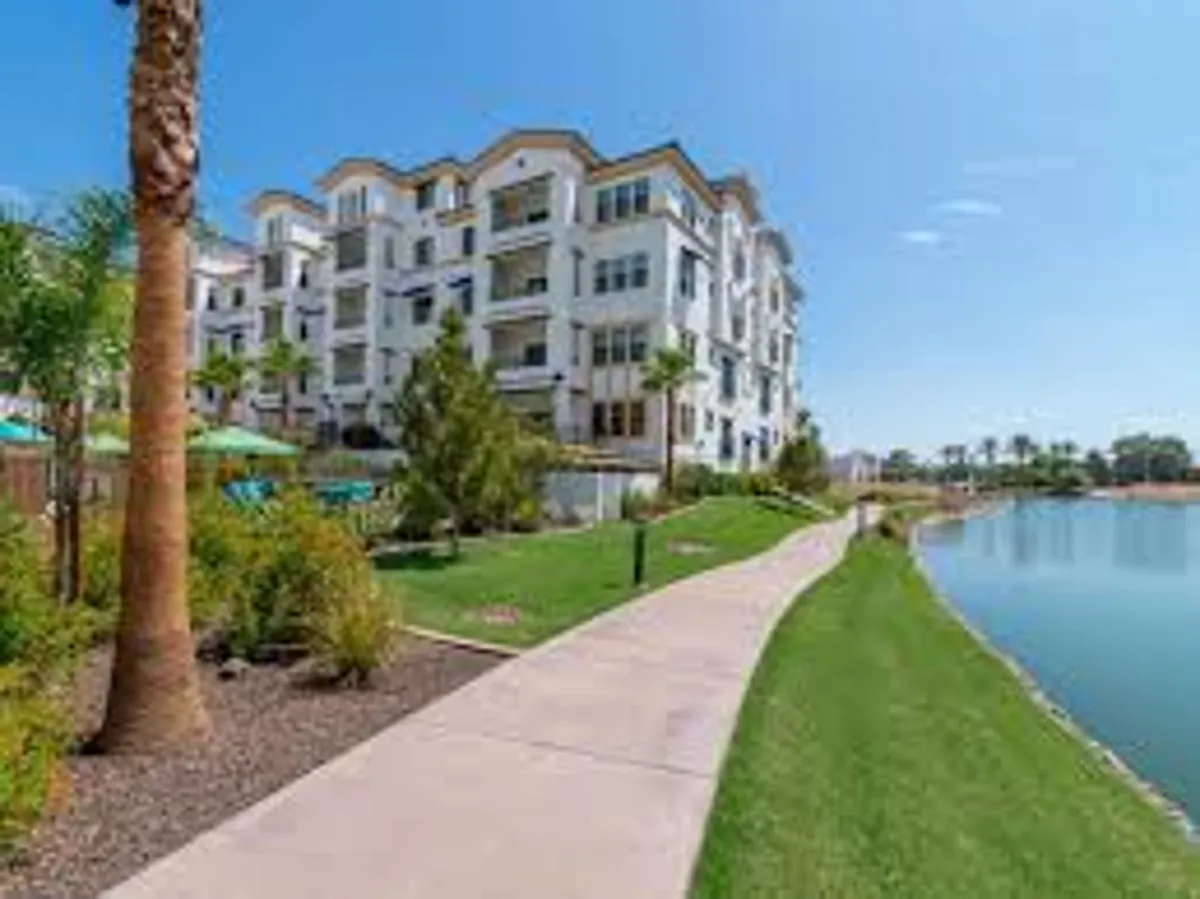A serene exterior view featuring a modern apartment building, a scenic walking path winding around a lake, and lush greenery all around. The environment is inviting for outdoor walks, jogs, and social gatherings by the water.
