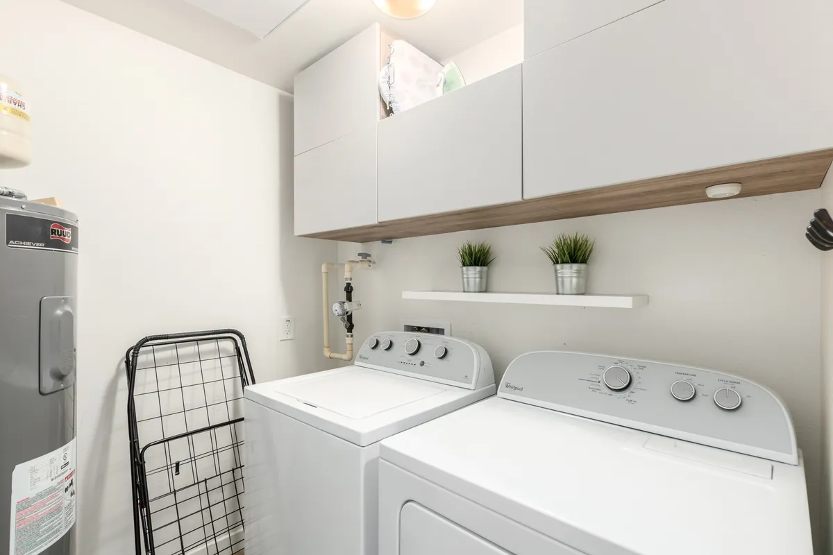 A tidy laundry room equipped with a washing machine, dryer, and a shelf adorned with plants. The space feels practical yet calming, emphasizing utility and comfort for longer stays.