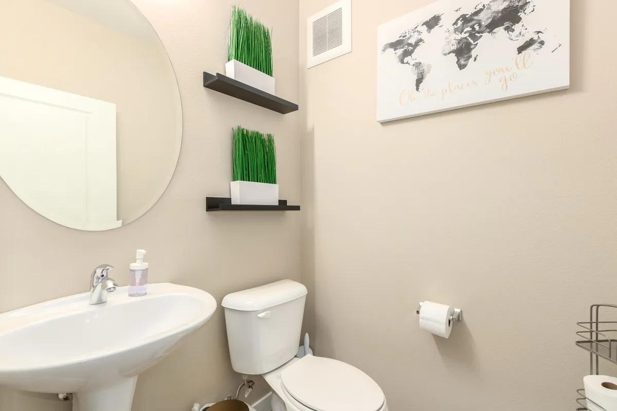 A half bath featuring a circular mirror, greenery on wall shelves, and thoughtful decor. The space feels fresh and inviting, perfect for guests.